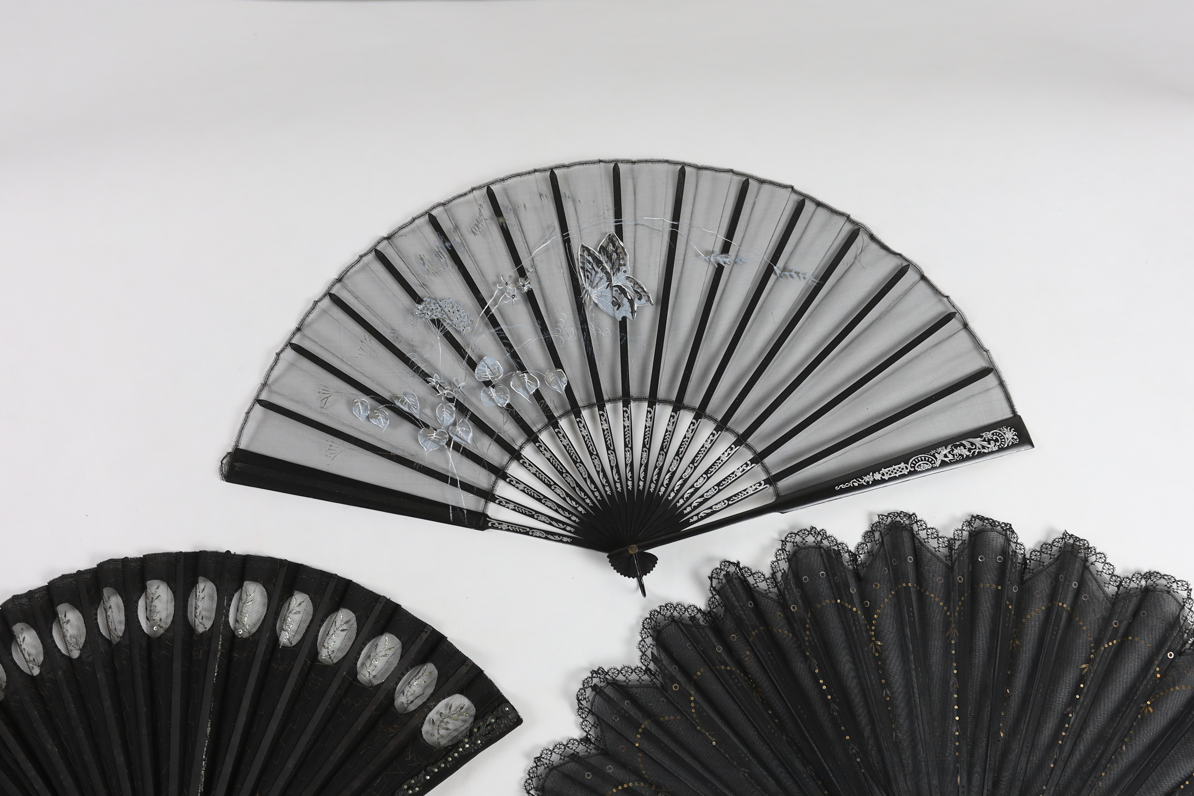 An Edwardian black silk and ornate sequin fan, a similar fan with carved ebony guards and a fine gauze fan with painted sprig and butterfly decoration (3)